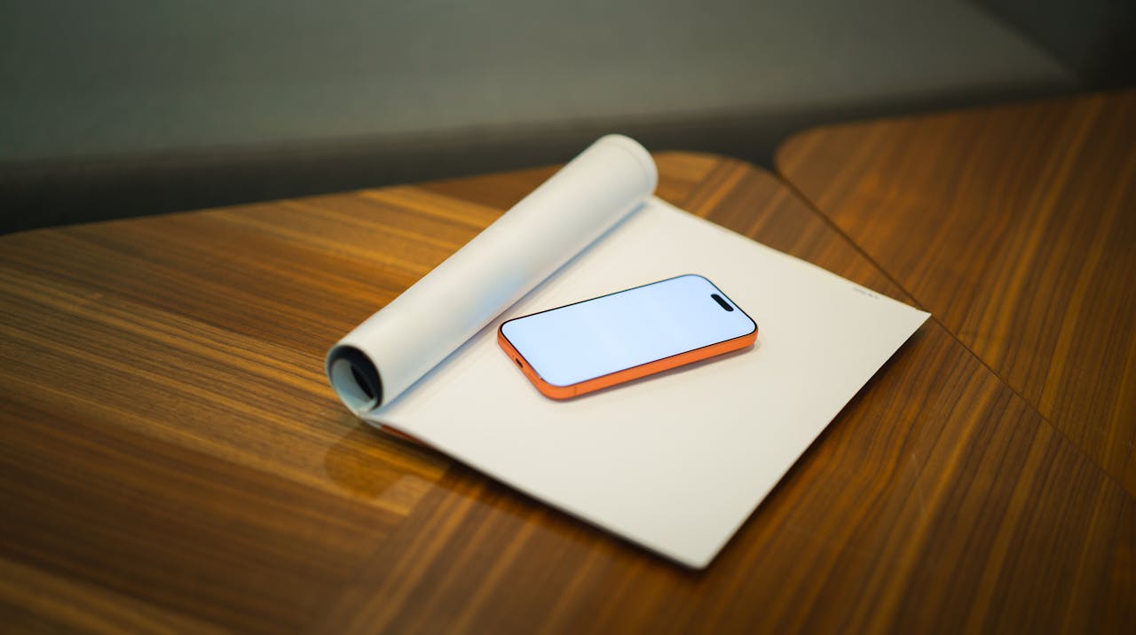 Modern workspace featuring a smartphone and roll of paper on a wooden desk, ideal for office presentations.
